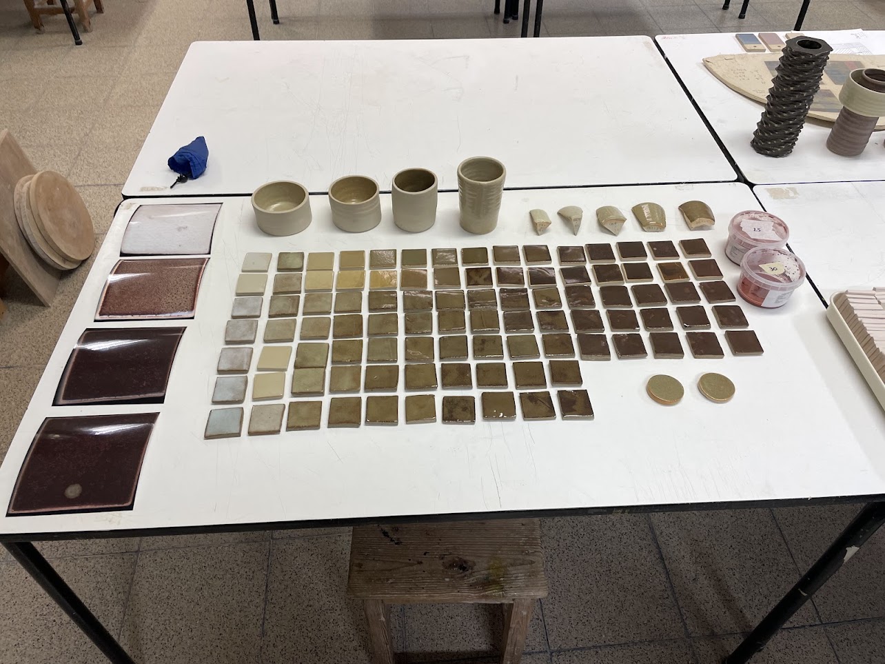 A spread of fired test tiles laid out on a table, together with some test cylinders and photo prints of tile scans.